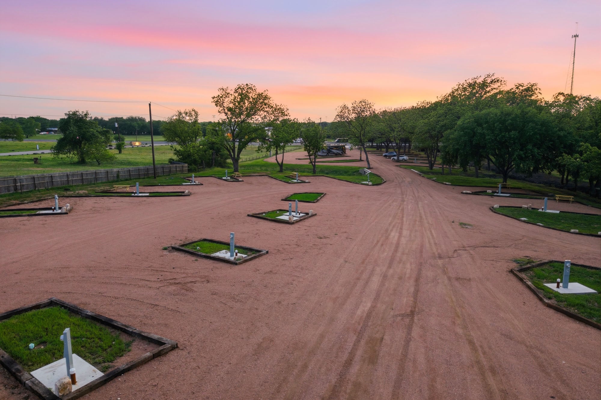 A row of empty RV parking spots with utility hookups on a gravel lot, surrounded by trees, at sunset.